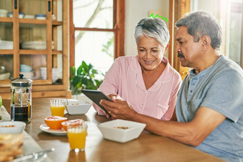 数字事情拍摄快乐的上了年纪的夫妇浏览数字平板电脑早餐表格首页