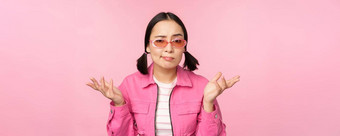 关闭肖像亚洲女孩困惑耸困惑相机穿太阳镜站粉红色的背景