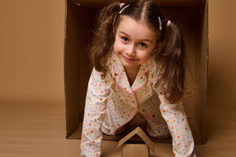 可爱的孩子女孩窥视纸板盒子相机工艺纸箱盒子米色背景复制空间广告住房保险真正的房地产概念