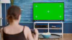 肩膀视图年轻的女人玩控制台视频游戏无线控制器绿色屏幕