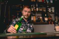 自信有胡子的酒保倒绿色酒瓶拍摄玻璃