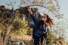 快乐的年轻的旅行女人太阳镜背包野营席数字相机带使灌木丛徒步旅行