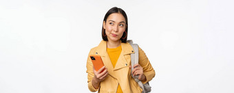 亚洲女孩旅行者背包持有移动电话智能手机应用程序深思熟虑的站白色背景