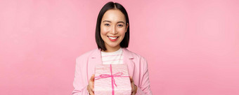 微笑亚洲女商人西装给礼物包装盒子站粉红色的背景