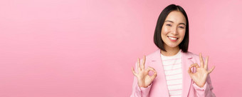 优秀的女商人企业西装显示批准手势推荐smth给积极的反馈微笑很高兴摆姿势粉红色的背景