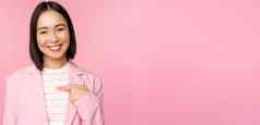 年轻的专业人微笑亚洲女商人女售货员指出手指自信摆姿势西装粉红色的背景
