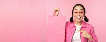 购物时尚的亚洲女孩太阳镜显示袋商店微笑<strong>推荐</strong>出售促销商店站粉红色的背景
