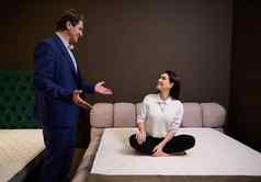 家具商店销售经理帮助美丽的女人客户端买家选择整形床垫好的姿势健康的睡眠