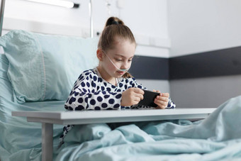 可爱的女孩玩游戏智能<strong>手机</strong>休息床上儿科医院房间
