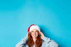 冬天假期圣诞节夏娃概念头可爱的红色头发的人女孩圣诞老人他底复制空间盯着标志站蓝色的背景