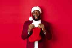 兴奋黑色的男人。开放圣诞节袜子礼物糖果微笑快乐站圣诞老人他红色的背景