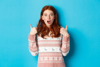 深刻的印象红色头发的人女孩毛衣显示竖起大拇指开放口着迷批准产品赞扬站蓝色的背景