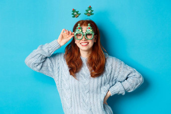 冬天假期圣诞节销售概念美丽的红色头发的人女模型庆祝一年穿有趣的聚会，派对头巾眼镜微笑相机