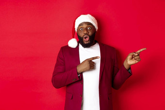 圣诞节聚会，派对假期概念兴奋黑色的男人。显示广告指出手指促销提供站圣诞老人他红色的背景