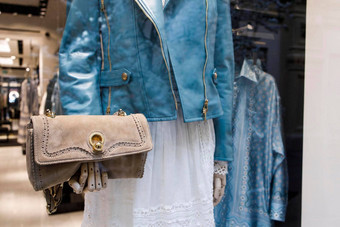 人体模型蓝色的皮革夹克持有米色仿麂皮离合器袋黄金配件商店窗口