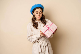 假期礼物概念美丽的女孩收到礼物盒子快乐持有粉红色的包装现在快乐的脸表达式米色背景