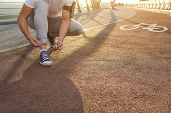 运动员跑步者系鞋带准备好了运行阳光下降城市桥跑步机有氧运动锻炼户外体育培训运动耐力健康的生活方式概念特写镜头
