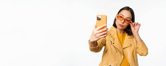 时尚的美丽的亚洲女孩太阳镜采取自拍智能手机摆姿势照片持有移动电话白色工作室背景