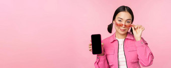 时尚的朝鲜文女孩年轻的女人太阳镜显示智能<strong>手机</strong>屏幕移动电话应用程序接口网站站粉红色的背景
