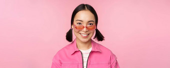 关闭时尚的朝鲜文女孩太阳镜微笑快乐摆姿势粉红色的背景人脸概念