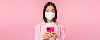 业务人科维德概念年轻的亚洲女商人西装医疗脸面具智能手机应用程序站粉红色的背景