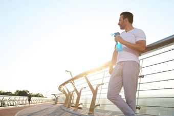 英俊的运动员运动员瓶水站现代玻璃城市桥放松有氧运动锻炼户外体育运动健身活跃的生活方式概念