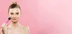 美概念特写镜头美丽的高加索人女人应用化妆化妆品粉刷完美的皮肤孤立的粉红色的背景复制空间