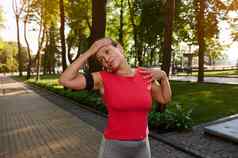 拉美裔运动女人紧红色的t恤智能手机持有人站城市公园伸展运动锻炼享受早....锻炼气候变暖身体早....慢跑