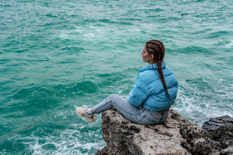 女人蓝色的夹克坐在岩石悬崖海狂风暴雨的海洋女孩旅行者休息认为梦想享受自然和平平静景观多风的天气