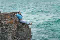 女人蓝色的夹克坐在岩石悬崖海狂风暴雨的海洋女孩旅行者休息认为梦想享受自然和平平静景观多风的天气