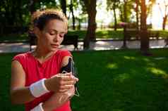 年轻的运动女人跑步者明亮的红色的t恤连接耳机移动电话集应用程序慢跑公园阳光明媚的夏天一天