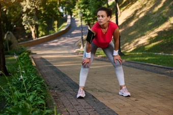 女跑步者拉美裔女运动员休息城市公园感觉疲惫慢跑跑步机温暖的阳光明媚的夏天一天身体重量培训减肥节食概念
