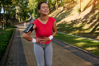 疲惫女人跑步者运动员紧运动服装智能手机持有人把手胃感觉抽筋一边运行跑步机城市公园体育运动受伤