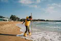 男孩黄色的橡胶靴子玩坚持沙子海滩学校孩子触碰水秋天冬天海孩子有趣的波海岸春天假期假期概念