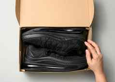女手持有棕色（的）纸板盒子黑色的体育运动鞋灰色的表格检查在线订单前视图