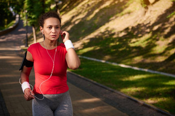 中间岁的确定女运动员跑步者听音乐耳机运行城市公园跑步机
