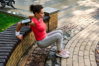 运动型活跃的中年非洲美国女人锻炼户外活跃的女运动员肱三头肌练习倾斜手木板凳上城市公园