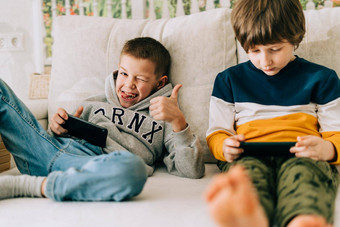 快乐的蔡尔兹男孩玩在线游戏看<strong>视频</strong>手机微笑孩子们有趣的移动应用程序享受<strong>免费</strong>的休闲时间首页沙发上兄弟玩电话