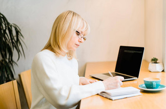 成熟的成人女人坐着咖啡馆咖啡杯子工作在线移动PC电脑女商人眼镜写作笔记本共同<strong>办公空间</strong>烤肉炉咖啡商店