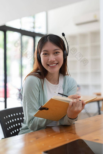 肖像年轻的亚洲女人耳机写作使列表采取笔记记事本工作学习移动PC在室内教育培训研讨会教育在线概念