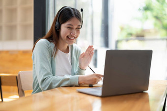 微笑女孩学生穿无线耳机研究在线老师快乐年轻的亚洲女人学习语言听讲座看网络研讨会写笔记移动PC坐咖啡馆遥远的教育