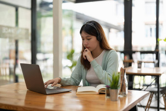 年轻的亚洲女人穿耳机研究在线看网络研讨会播客移动PC听学习教育会议调用使笔记坐工作桌子上网络学习概念