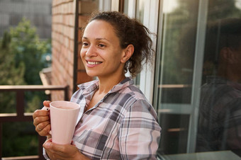 宁静美丽的黑头发的女人微笑露出牙齿的微笑享受早....咖啡阳台