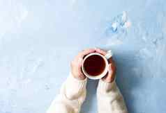 女人持有杯热茶蓝色的表格手温暖的毛衣杯子冬天早....