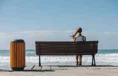 年轻的美丽的女人坐着板凳上海滩蓝色的海洋