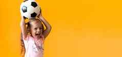 真实的可爱的微笑学前教育女孩经典黑色的白色足球球相机黄色的背景孩子玩足球t恤短裤体育运动冠军团队概念
