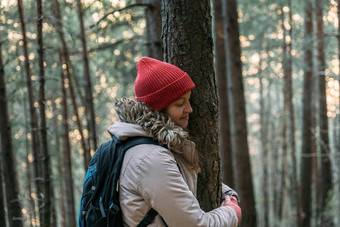 旅游年轻的女人关闭眼睛红色的帽拥抱树冷森林山徒步旅行连接自然保护环境概念