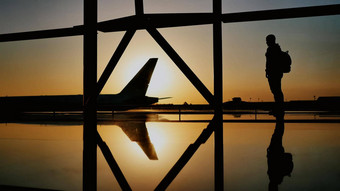 轮廓旅游的家伙看起飞飞机通过巨大的飞机站机场窗口日落晚上旅行概念人机场