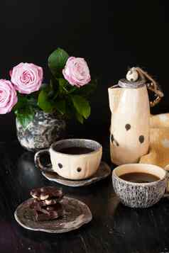 杯黑色的咖啡黑色的巧克力黄色的茶壶花瓶粉红色的玫瑰黑暗背景