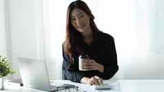 微笑亚洲女商人持有咖啡杯子移动PC办公室相机